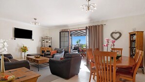 Een woonkamer met een bank, salontafel, televisie en een eethoek met stoelen en een tafel.