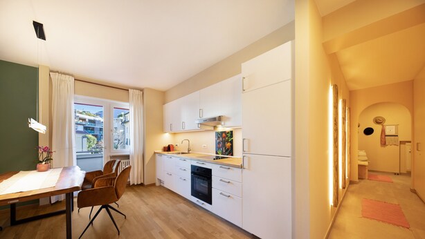 A modern kitchen with white cabinets, a dining area with a table and chairs, and a view of the outside. - Apartment Huita with Balcony and Wi-Fi (Bozen)