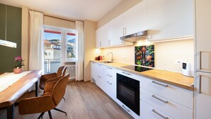 A modern kitchen with a wooden countertop, white cabinets, a built-in oven, and a window with a view of buildings. - Apartment Huita with Balcony and Wi-Fi (Bozen)