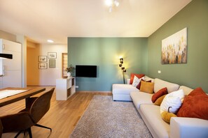 A modern living room with a sofa, a flat-screen TV, a dining area with a table and chairs, and a kitchen area. - Apartment Huita with Balcony and Wi-Fi (Bozen)