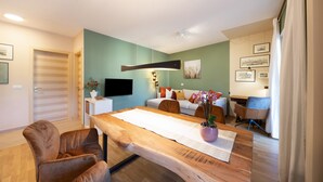 A modern living room with a wooden dining table, brown leather chairs, a sofa, and a TV mounted on the wall. - Apartment Huita with Balcony and Wi-Fi (Bozen)