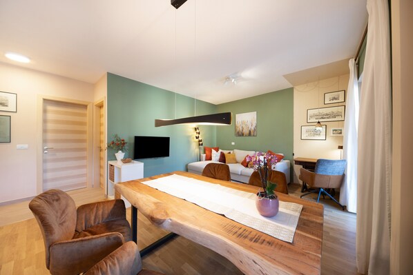 A modern living room with a wooden dining table, brown leather chairs, a sofa, and a TV mounted on the wall.