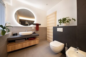 A modern bathroom with a round mirror, a white sink, a toilet, and a bidet. - Apartment Huita with Balcony and Wi-Fi (Bozen)