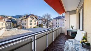 A balcony with a view of buildings and mountains, a table with a tablecloth, and a potted plant. - Apartment Huita with Balcony and Wi-Fi (Bozen)