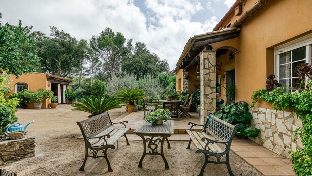 Un patio al aire libre con paredes de piedra, una mesa de piedra y bancos de madera.