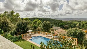Una piscina con borde curvo, rodeada por una barandilla amarilla y una pequeña terraza con mesa y sillas.