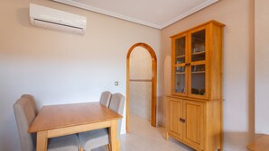 A dining area with a wooden table and chairs, a cabinet with glass doors, and an air conditioning unit on the wall. - Vacation Apartment "Playa Golf 2" with Wi-Fi, Garden & Terrace (Cabo Roig)