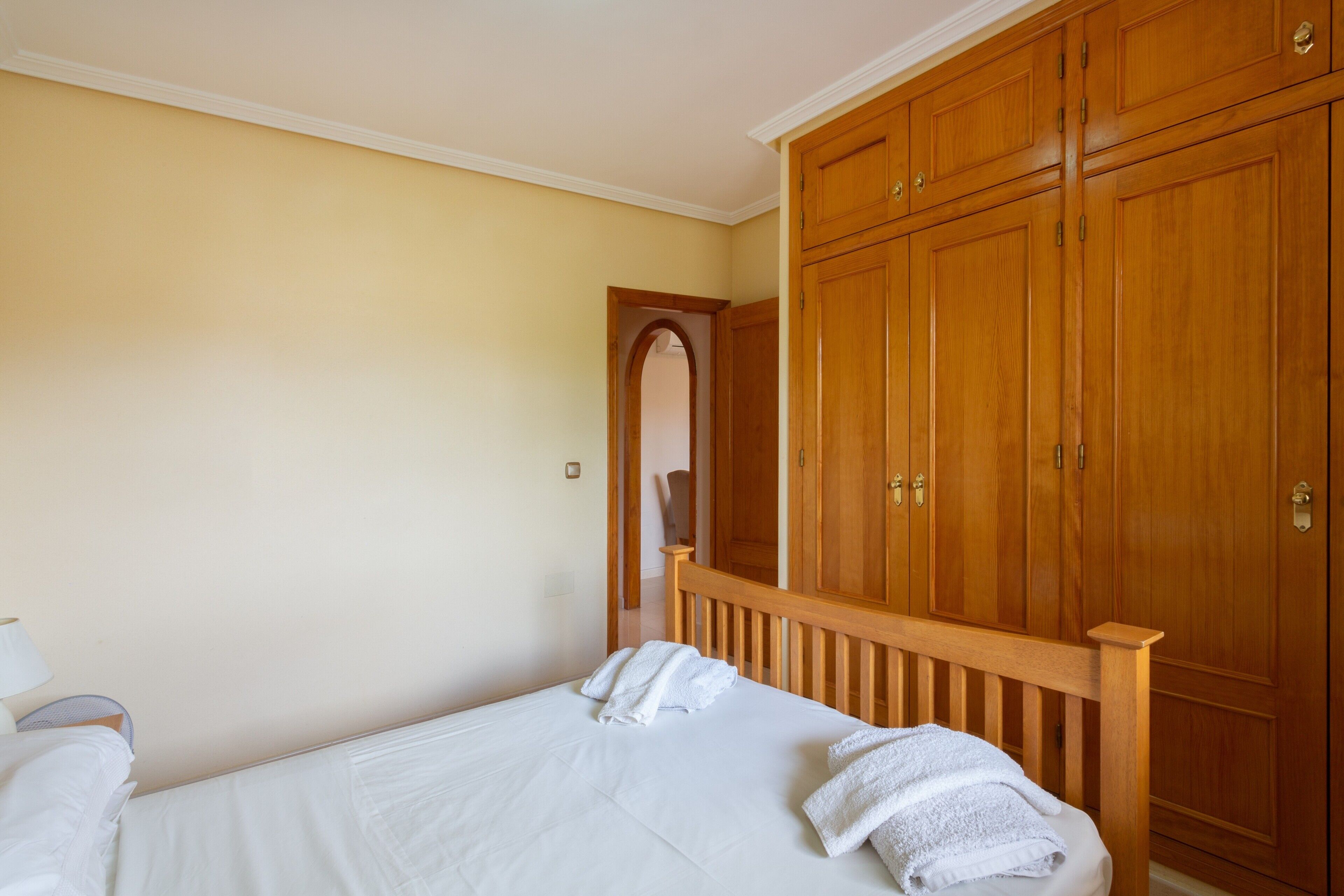 A bedroom with a bed, a wooden wardrobe, and a door leading to another room.