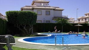 A swimming pool with a bench, surrounded by greenery and a building with a tiled roof. - Vacation Apartment "Playa Golf 2" with Wi-Fi, Garden & Terrace (Cabo Roig)