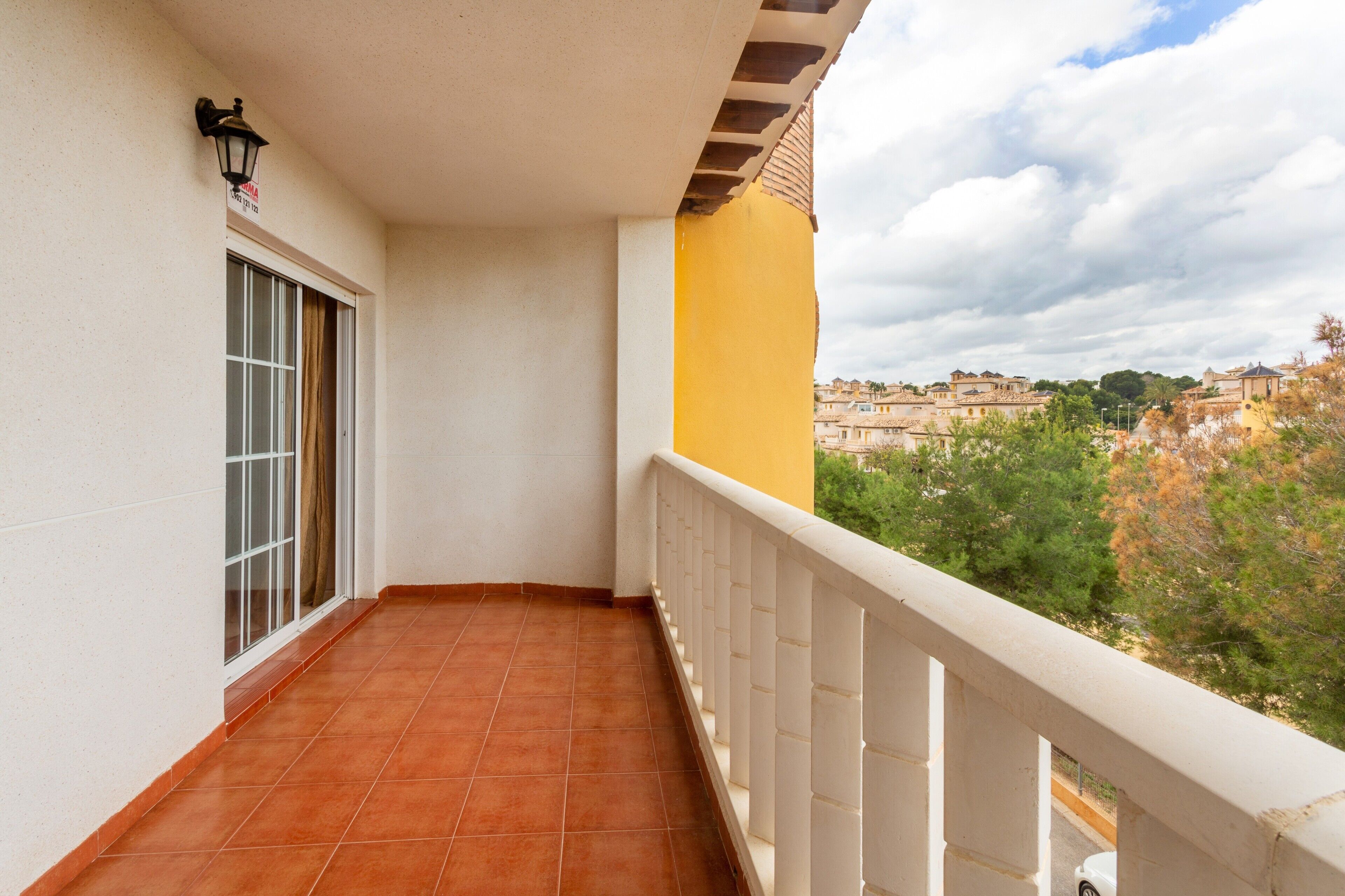 Ein Balkon mit gefliestem Boden, einem weißen Geländer und einem Fenster mit Vorhang.