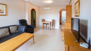 A living room with a sofa, a wooden table, a TV, and a dining area with chairs. - Vacation Apartment "Playa Golf 2" with Wi-Fi, Garden & Terrace (Cabo Roig)