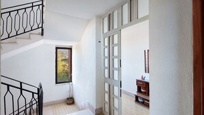 A staircase with a metal railing, a potted plant, a door with glass panels, and a wooden cabinet with decorative items. - Holiday Apartment 'Casa Isabea' with Sea View, 2 Balconies, Garden & Wi-Fi (Pozzuoli)