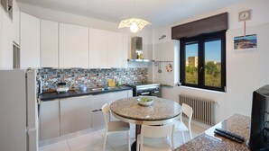 A kitchen with a round table, white chairs, a stove, and a window with a view. - Holiday Apartment 'Casa Isabea' with Sea View, 2 Balconies, Garden & Wi-Fi (Pozzuoli)