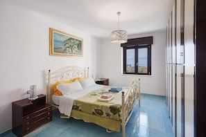 A bedroom with a bed, a nightstand, a dresser, a window with a view, and a hanging light fixture.