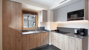 A modern kitchen with wooden cabinets, a built-in microwave, and a window with a stone wall view. - Mountain Apartment - Rasia Residence Relax (Livigno)