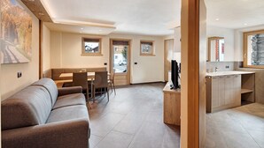 A modern interior with a sofa, dining area, kitchen, and a view through a door. - Mountain Apartment - Rasia Residence Relax (Livigno)