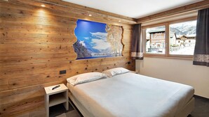 Une chambre d’hôtel avec un mur en bois, un lit, une petite table de chevet et une fenêtre donnant sur une montagne.