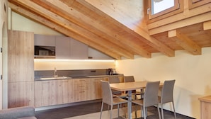 A modern kitchen with wooden beams, a dining area with a table and chairs, and a view of the kitchen through a window.