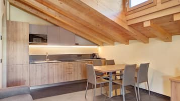 A modern kitchen with wooden beams, a dining area with a table and chairs, and a view of the kitchen through a window.