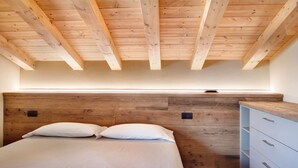 A bedroom with a wooden ceiling, a bed with white bedding, a wooden headboard, and a white dresser with drawers.