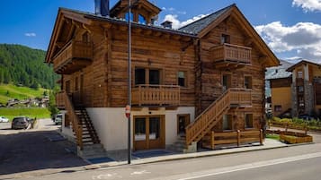 A wooden chalet with a balcony, a staircase, and a view of the surrounding landscape.