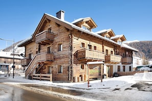 Una cabaña de madera con balcones, un cartel que dice 'Hotel Rasina' y una montaña nevada al fondo.