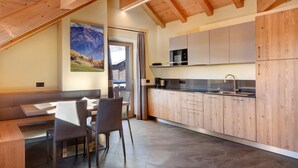 A modern kitchen with wooden cabinets, a dining area with a bench, and a view of mountains through a window. - Night Apartment – Rasia Residence Relax with Balcony and Wellness Area (Livigno)