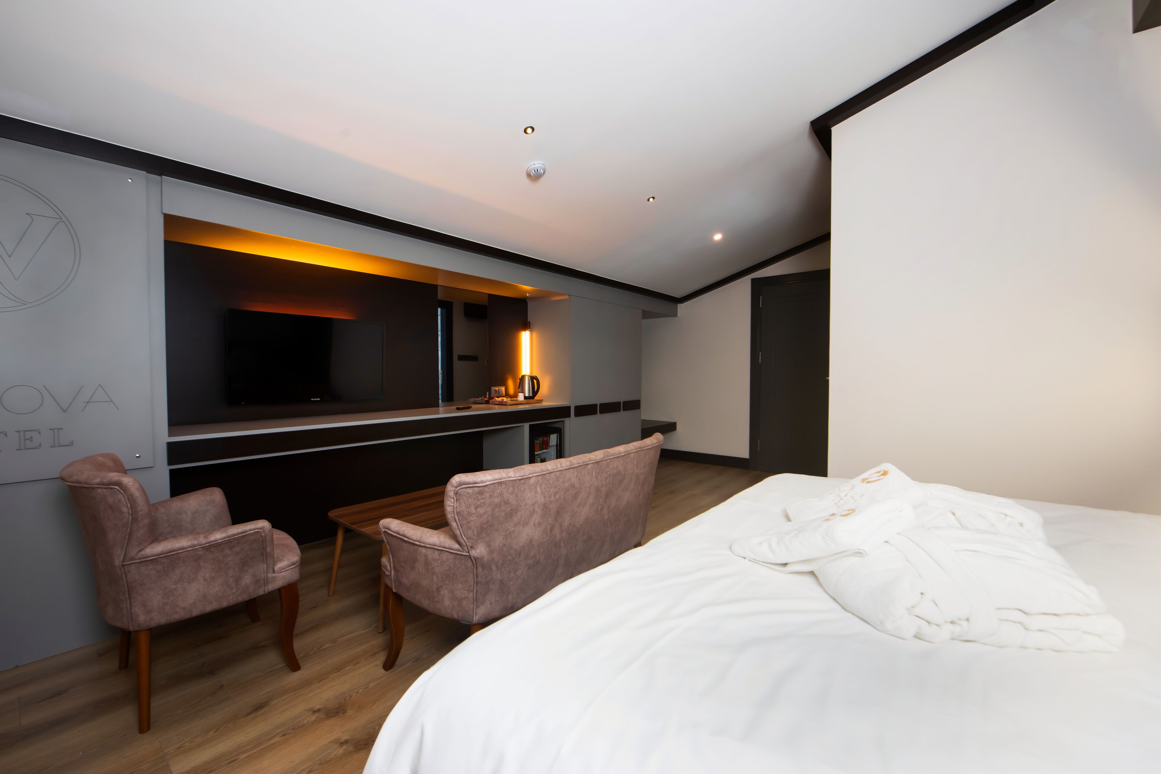 Una habitación de hotel moderna con una cama grande, dos sillones, un escritorio pequeño y un televisor.