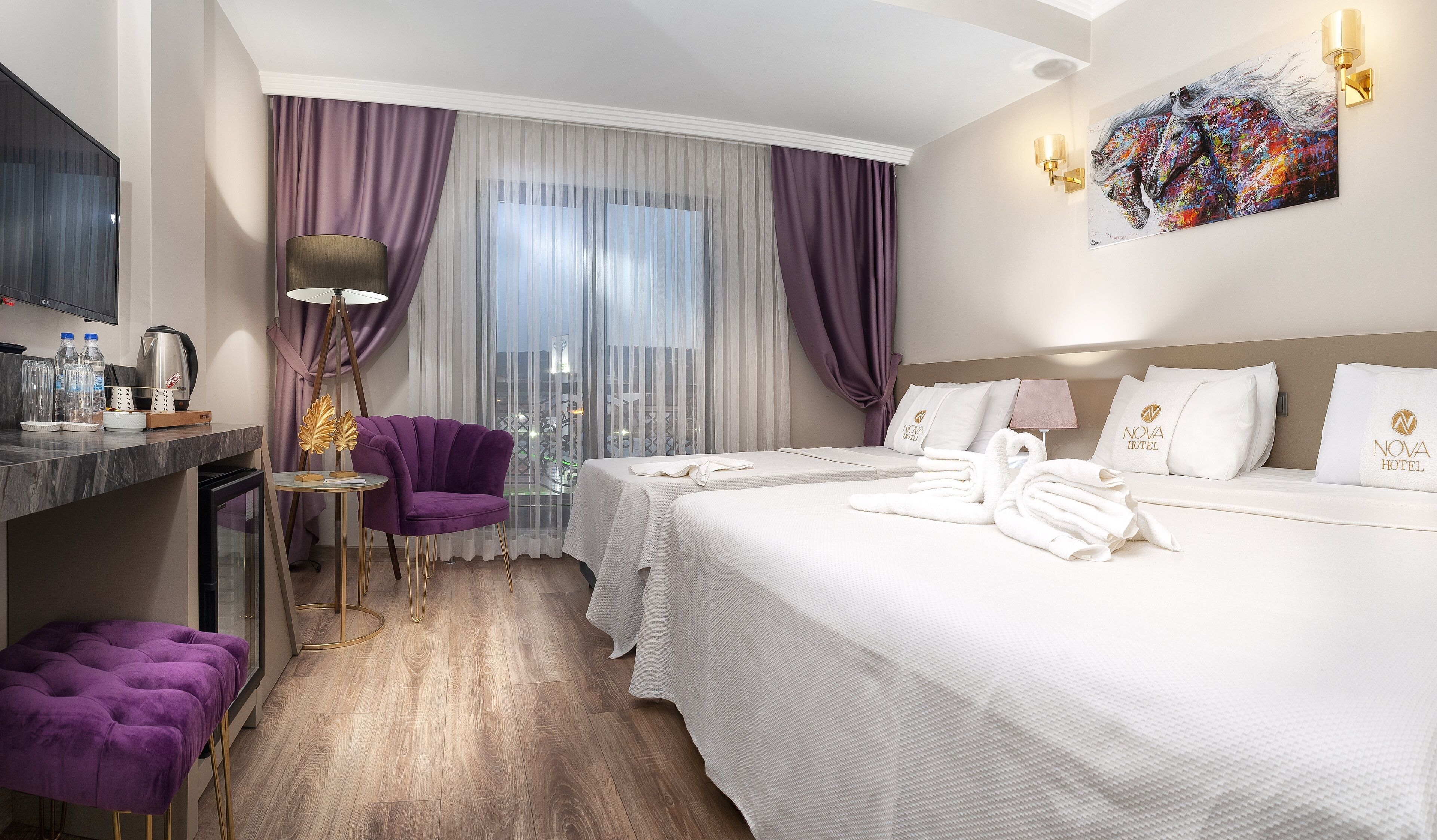 A hotel room with a bed, a chair, a desk with a lamp, and a painting on the wall.