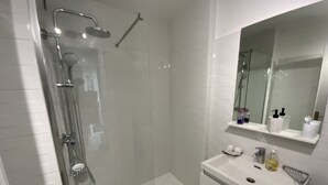 Ein modernes Badezimmer mit einer gläsernen Dusche, einem weißen Waschbecken mit Spiegel darüber und einer kleinen Ablage für Toilettenartikel.