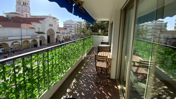 Ein Balkon mit Blick auf historische Gebäude, einem Tisch mit Stühlen und einem blauen Sonnensegel.