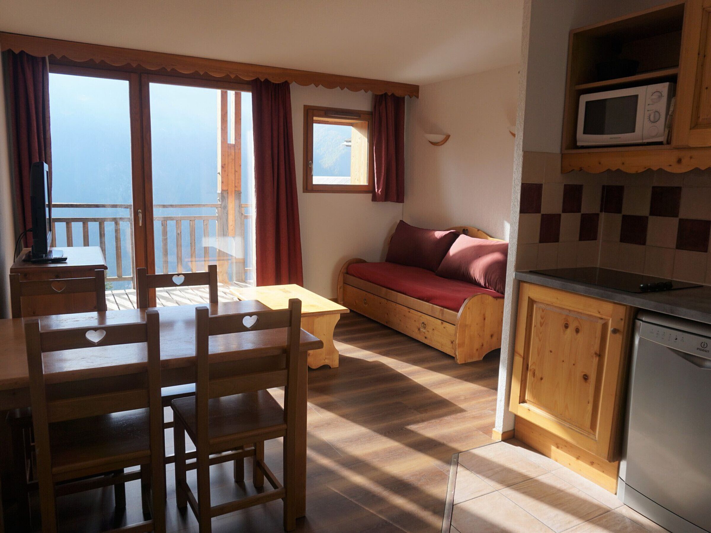 Ein gemütliches Zimmer mit Holztisch, Stühlen, einer Couch und einer Küchenzeile inklusive Mikrowelle und Geschirrspüler.
