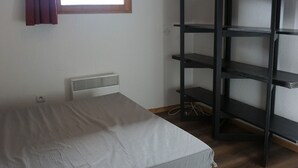 Ein Schlafzimmer mit einem Bett, einem Heizkörper, einem Fenster mit Vorhängen und einer schwarzen Regaleinheit.
