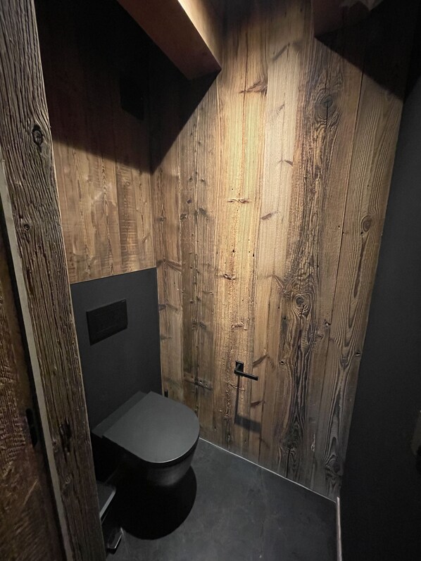 A small, compact bathroom with a wooden wall, a toilet, and a shower area.