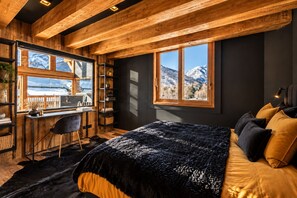 A bedroom with a bed, a desk, and a view of mountains through large windows.