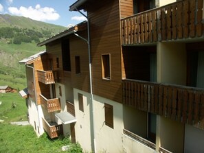 A multi-story building with wooden balconies and a view of a green valley. - 3-bedroom duplex, 8 people, pets allowed, parking, near slopes (Orcières Merlette)