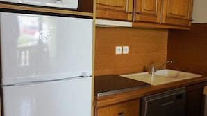 Eine kleine Küche mit einem weißen Kühlschrank, einer Spüle, Holzschränken und einem Geschirrspüler.