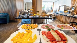 A buffet with various fruits, meats, and a coffee station.