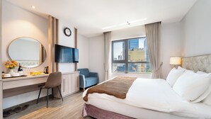 A hotel room with a bed, desk, chair, TV, and a large window with a city view.