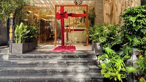 A hotel entrance with a red curtain, steps leading up to it, and surrounding greenery.