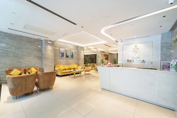 A modern hotel lobby with a reception desk, sofas, and a dining area.