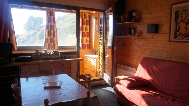 A cozy room with a wooden interior, a dining table with chairs, a pink sofa, and a window with curtains. - Studio cabin for 4 with view, near ski lift (Orcières Merlette)