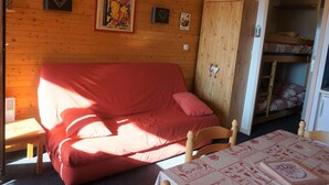 A cozy room with a wooden wall, a red sofa, a wooden wardrobe, and a bunk bed with a ladder. - Studio cabin for 4 with view, near ski lift (Orcières Merlette)