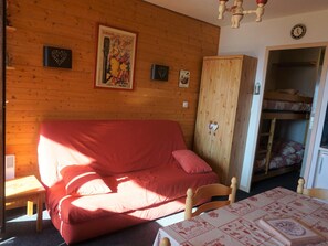 Ein gemütliches Zimmer mit einer Holzwand, einem roten Sofa, einem Holzschrank und einem Stockbett mit einer Leiter.