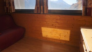 A room with wooden walls, a window with curtains, a red sofa, and a wooden dresser. - Studio cabin for 4 with view, near ski lift (Orcières Merlette)