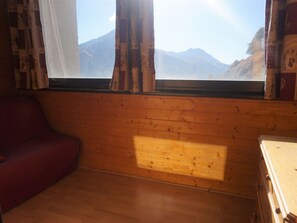 Ein Zimmer mit Holzwänden, einem Fenster mit Vorhängen, einem roten Sofa und einer Holzkommode.