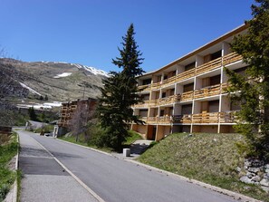Een hotel met meerdere verdiepingen, balkons, een berg op de achtergrond en een weg in de voorgrond.