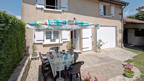 A two-story house with a patio area featuring a table set for dining, surrounded by chairs. - Cozy cottage with pets allowed and wifi in Saint-Jean-la-Vêtre (Saint-Jean-la-Vêtre)