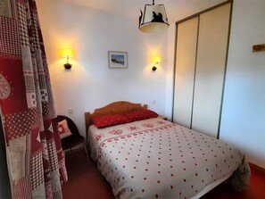Camera da letto con un letto, due lampade a parete, una testiera in legno, un armadio e una tenda con motivi patchwork.