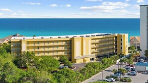 Un hotel de varios pisos con balcones, una zona de estacionamiento y vistas al océano.